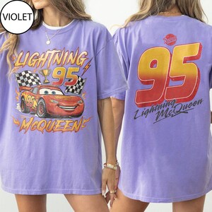 K&ouml;nnte beinhalten: Ein helllila T-Shirt mit einem Lightning McQueen-Motiv aus dem Film Cars. Auf der Vorderseite steht "Lightning 95 McQueen" mit einem Cartoon-Rennwagen. Auf der R&uuml;ckseite des Shirts befindet sich eine gro&szlig;e "95"-Grafik.