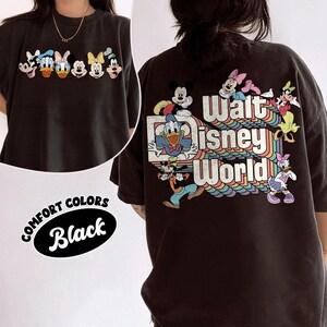 Pu&ograve; includere: T-shirt nera Comfort Colors con personaggi Disney sul davanti e sul retro. Il davanti mostra Topolino, Paperino, Paperina, Minnie e Pippo. Il retro presenta Topolino, Paperino e altri personaggi con la scritta "Walt Disney World".