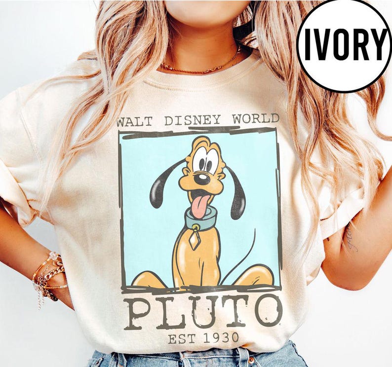 Puede incluir: Sudadera de color marfil con un dise&ntilde;o de Pluto de Walt Disney World. El dise&ntilde;o incluye la imagen de Pluto, las palabras "WALT DISNEY WORLD" y "PLUTO EST 1930" en un marco rectangular. La sudadera tiene mangas largas.