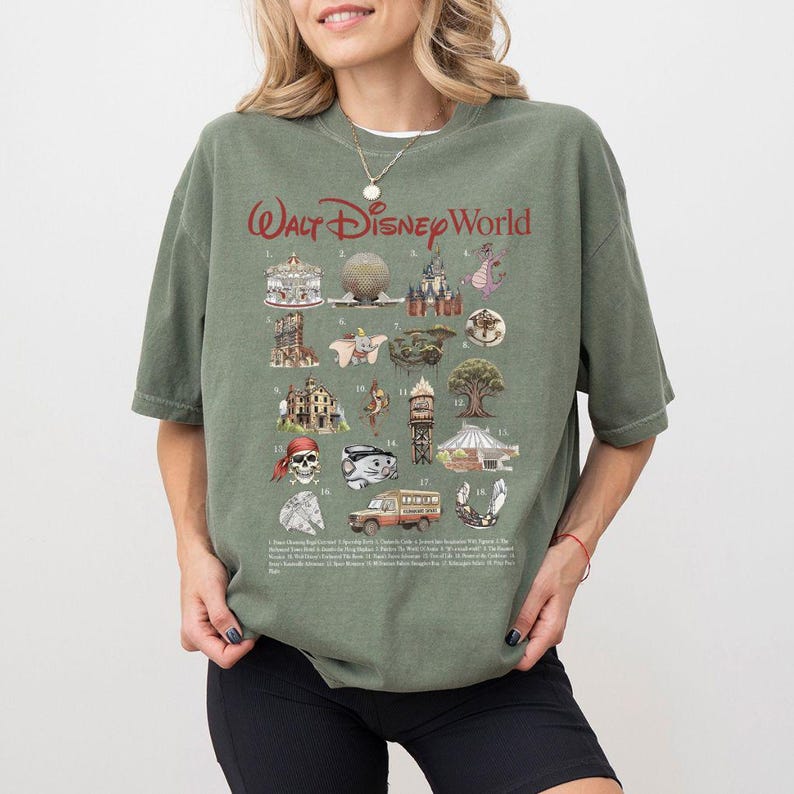 Puede incluir: Una camiseta verde oliva con el texto "Walt Disney World" en rojo. La camiseta muestra ilustraciones de atracciones de Disney World, como un carrusel, Spaceship Earth y el castillo de Cenicienta.