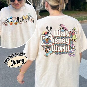 Pu&ograve; includere: T-shirt color avorio con personaggi Disney sul davanti e sul retro. Il davanti mostra facce di cartoni animati, mentre il retro presenta "Walt Disney World" con Topolino, Paperino e altri personaggi. La maglietta ha un girocollo e maniche corte.