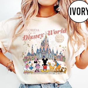 Puede incluir: Sudadera de color marfil con un gr&aacute;fico colorido de Disney World en Florida. El dise&ntilde;o incluye el logotipo de Disney World, el castillo y varios personajes de Disney. Tambi&eacute;n est&aacute; presente el texto "Florida Est. 1971".
