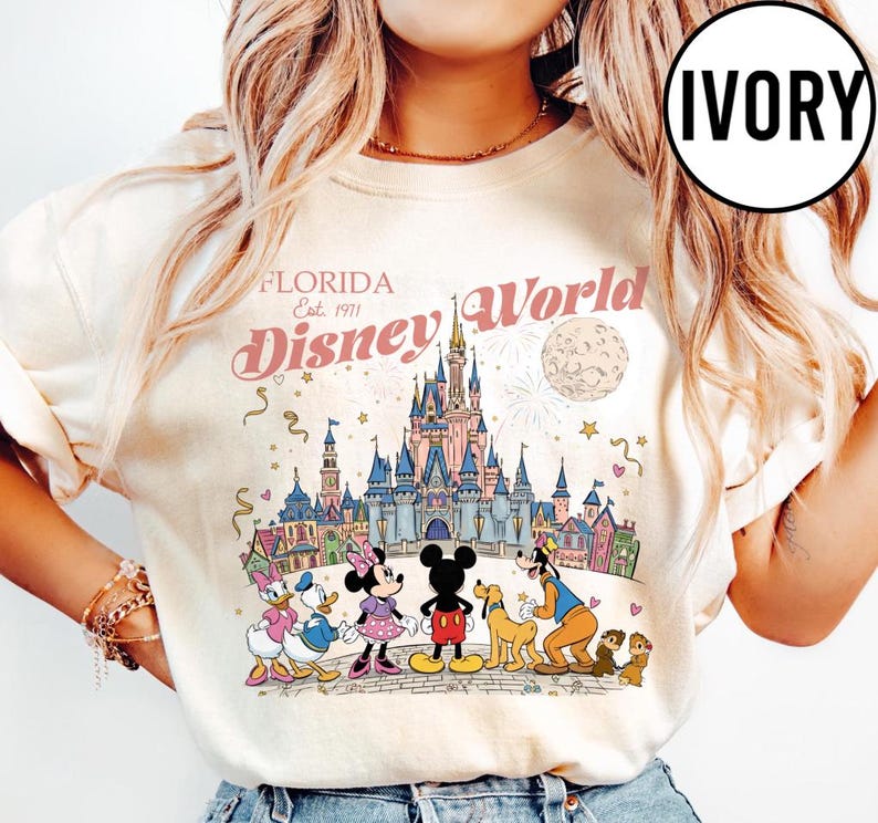 Puede incluir: Sudadera de color marfil con un gr&aacute;fico colorido de Disney World en Florida. El dise&ntilde;o incluye el logotipo de Disney World, el castillo y varios personajes de Disney. Tambi&eacute;n est&aacute; presente el texto "Florida Est. 1971".