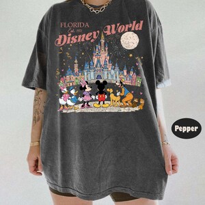Puede incluir: Camiseta gris oscuro con un gr&aacute;fico colorido de Disney World en Florida. El dise&ntilde;o incluye a Mickey y Minnie Mouse, el Pato Donald, Goofy y un castillo. El texto "Florida Disney World Est. 1971" est&aacute; impreso encima del gr&aacute;fico.