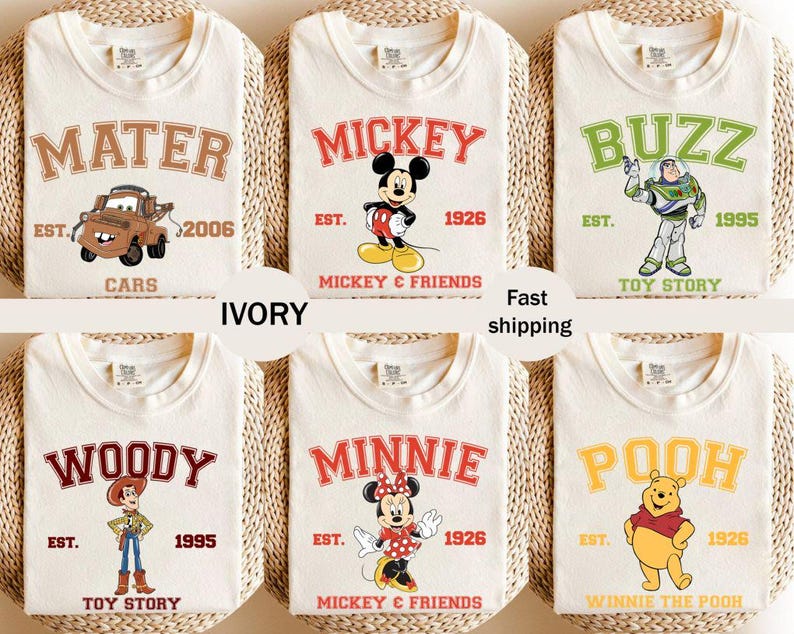 May include: Ivory-colored t-shirts featuring various cartoon characters and text. Designs include "Mater" with a car, "Mickey" with Mickey Mouse, "Buzz" with Buzz Lightyear, "Woody" with Woody, "Minnie" with Minnie Mouse, and "Pooh" with Winnie the Pooh.