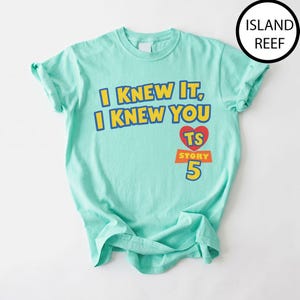 May include: A light mint green short-sleeve t-shirt featuring the yellow text I KNEW IT, I KNEW YOU with a red heart containing the letters TS above the orange text STORY and the large yellow number 5. The shirt has a crew neckline.
