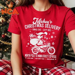 May include: Red t-shirt with a white graphic of Mickey Mouse on a motorbike, carrying gifts. The text says "Mickey's Christmas Delivery" and "North Pole to Main Street Express". A festive design for Christmas.
