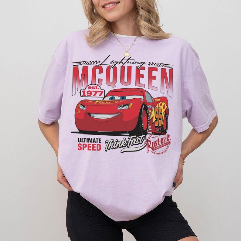Puede incluir: Camiseta lila claro con un dise&ntilde;o de Lightning McQueen, el personaje de la pel&iacute;cula Cars. El dise&ntilde;o incluye el texto "Lightning McQueen" y "est. 1977", adem&aacute;s de las palabras "Ultimate Speed" y "Think Fast".