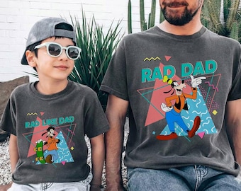 May include: Two matching charcoal gray t-shirts with the text "RAD DAD" and "RAD LIKE DAD" featuring a cartoon character. The shirts have a retro 80s design with geometric shapes and a cartoon character.