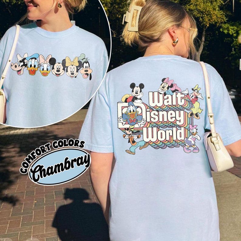 Pu&ograve; includere: T-shirt azzurra con personaggi Disney. La parte anteriore presenta Topolino, Paperino e altri personaggi. Il retro ha la scritta "Walt Disney World" con un design arcobaleno e altri personaggi.