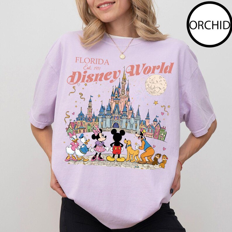 Puede incluir: Camiseta lila claro con un gr&aacute;fico colorido de Disney World en Florida. El dise&ntilde;o incluye el texto "Florida Disney World Est. 1971" y personajes de Disney como Mickey y Minnie Mouse y Donald Duck.