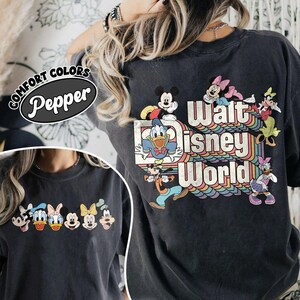 Pu&ograve; includere: T-shirt grigio scuro con la scritta "Walt Disney World" in un design arcobaleno retr&ograve;, con personaggi dei cartoni animati come Topolino e Paperino. La maglietta ha anche la scritta "Comfort Colors Pepper" in un ovale nero.