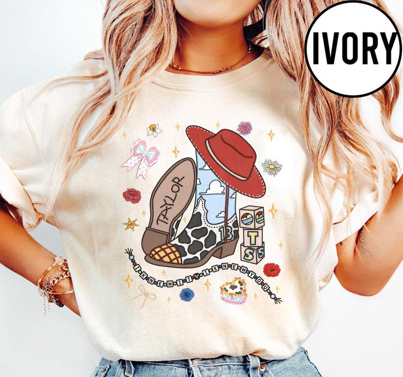 May include: An ivory t-shirt featuring a graphic print of a cowboy boot with a cow print pattern, a red hat, a stack of blocks with the letters T, S, and the number 13, a bow, flowers, and a beaded string with the text I KNEW IT WHEN YOU.
