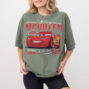 Puede incluir: Camiseta verde con un dise&ntilde;o de Rayo McQueen de la pel&iacute;cula Cars. El dise&ntilde;o incluye el texto "Lightning McQueen", "Ultimate Speed" y "Think Fast". El gr&aacute;fico del coche rojo est&aacute; sobre un fondo rojo y blanco.