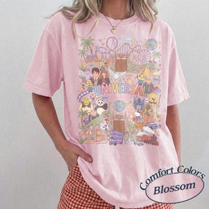 Może przedstawiać: Jasnor&oacute;żowy t-shirt z kr&oacute;tkim rękawem z kolorowym nadrukiem graficznym przedstawiającym postacie i punkty orientacyjne Universal Studios. Wz&oacute;r zawiera r&oacute;żne animowane postacie, kolejkę g&oacute;rską oraz napis UNIVERSAL dużymi, wielokolorowymi literami.