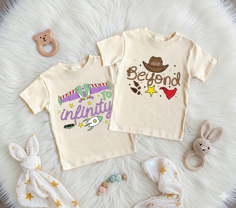 Puede incluir: Dos camisetas crema de manga corta con dise&ntilde;os gr&aacute;ficos. Una camiseta presenta una nave espacial morada y verde con el texto "To infinity". La otra camiseta tiene un sombrero de vaquero marr&oacute;n y el texto "and Beyond".