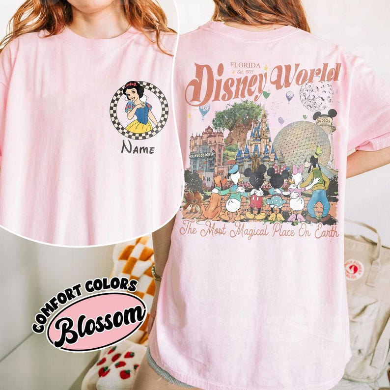 May include: A pale pink t-shirt with a Snow White graphic and the word "Name". The back of the shirt has a Disney World design with characters and the text "The Most Magical Place On Earth".