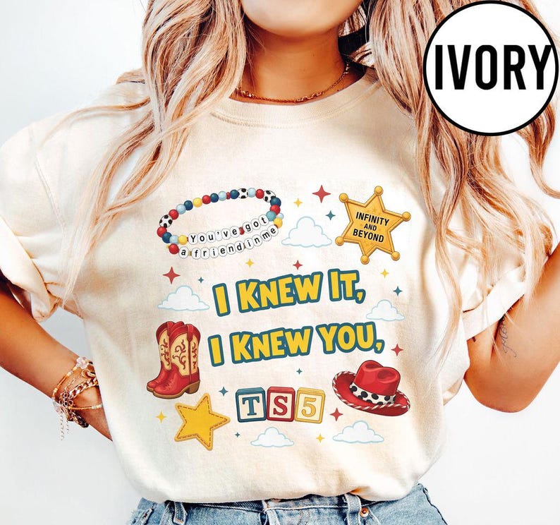May include: An ivory t-shirt featuring a graphic print with a beaded bracelet reading "You've got a friend in me," a gold sheriff star badge, red cowboy boots, a red cowboy hat, and blocks spelling "TS5." Text reads "I KNEW IT, I KNEW YOU."