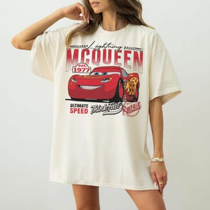 Puede incluir: Camiseta color crema con un gr&aacute;fico de Rayo McQueen de la pel&iacute;cula Cars. El dise&ntilde;o incluye el texto "Lightning McQueen est. 1977", "Ultimate Speed" y "Think Fast". El coche rojo es el punto focal.