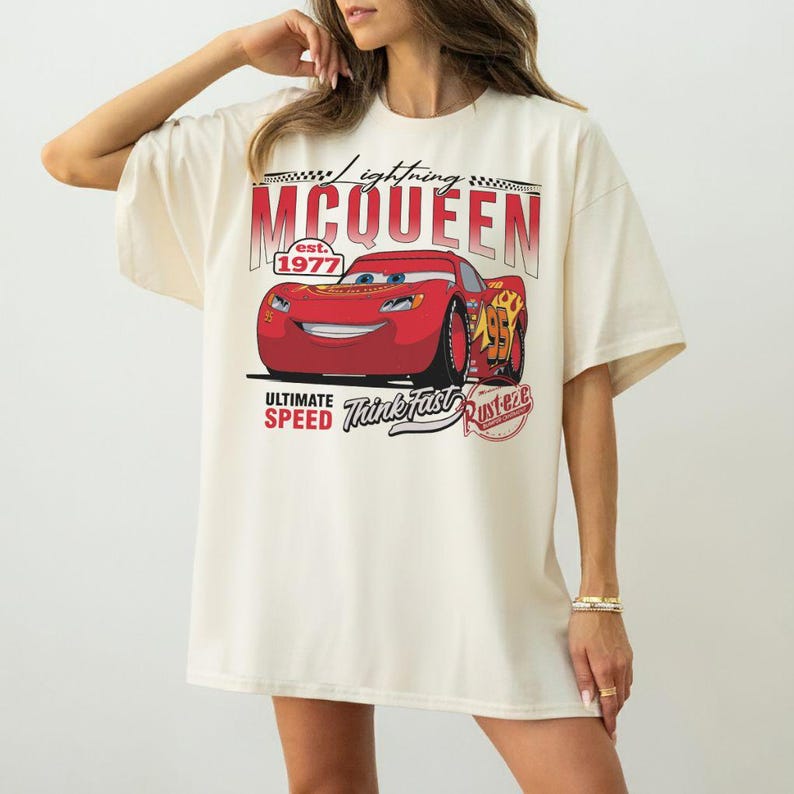 Puede incluir: Camiseta color crema con un gr&aacute;fico de Rayo McQueen de la pel&iacute;cula Cars. El dise&ntilde;o incluye el texto "Lightning McQueen est. 1977", "Ultimate Speed" y "Think Fast". El coche rojo es el punto focal.