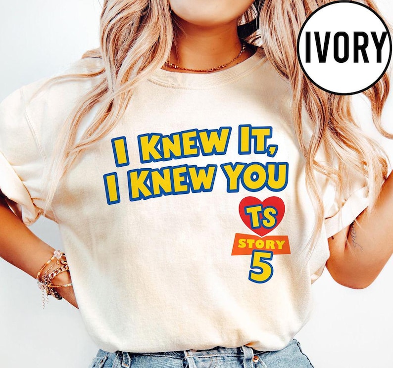 May include: An ivory t-shirt featuring the yellow text I KNEW IT, I KNEW YOU with blue outlines. Below the text is a red heart containing the yellow letters TS, followed by the orange text STORY and the large blue number 5 with a yellow outline.
