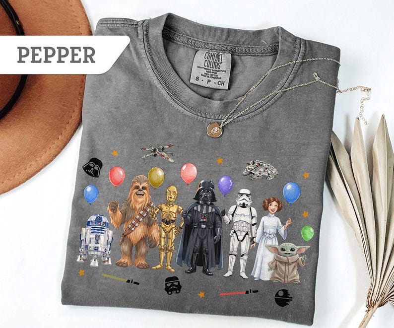 May include: Gray t-shirt featuring Star Wars characters and balloons. The design includes Darth Vader, Chewbacca, R2-D2, and other characters. The shirt has a crew neck and short sleeves. The word "PEPPER" is in a white banner.