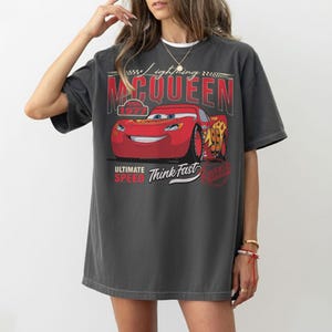 Puede incluir: Camiseta gris oscuro con un gr&aacute;fico de Rayo McQueen de la pel&iacute;cula Cars. El dise&ntilde;o incluye el texto "Lightning McQueen", "95", "Ultimate Speed" y "Think Fast". La camiseta tiene un aspecto vintage y desgastado.