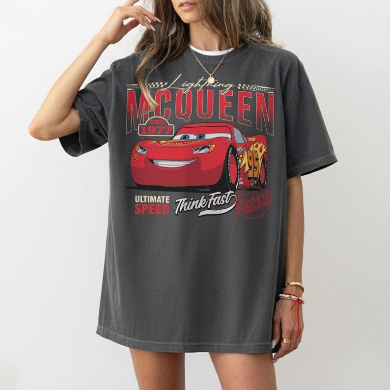 Puede incluir: Camiseta gris oscuro con un gr&aacute;fico de Rayo McQueen de la pel&iacute;cula Cars. El dise&ntilde;o incluye el texto "Lightning McQueen", "95", "Ultimate Speed" y "Think Fast". La camiseta tiene un aspecto vintage y desgastado.