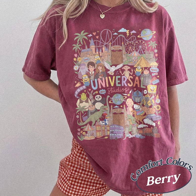 Może przedstawiać: Jagodowy t-shirt z kr&oacute;tkim rękawem z wielokolorowym nadrukiem graficznym przedstawiającym r&oacute;żne postacie animowane i zabytki Universal Studios. Wz&oacute;r zawiera napis Universal Studios oraz r&oacute;żnorodne postacie z bajek.