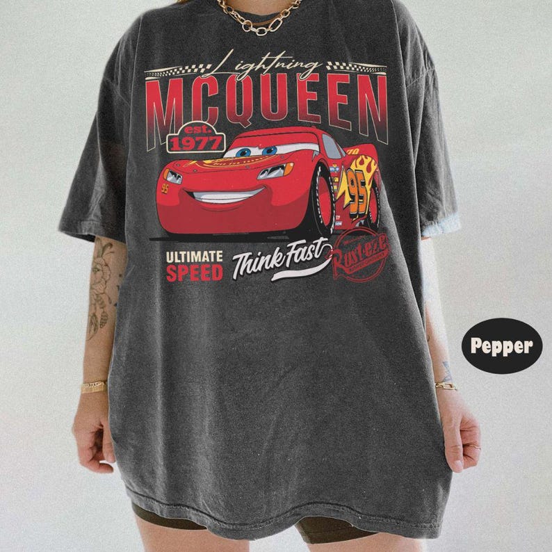 Puede incluir: Camiseta gris oscuro con un dise&ntilde;o de Rayo McQueen de la pel&iacute;cula Cars. El dise&ntilde;o incluye el texto "Lightning McQueen" y "Ultimate Speed Think Fast". El n&uacute;mero 95 es visible en el coche.