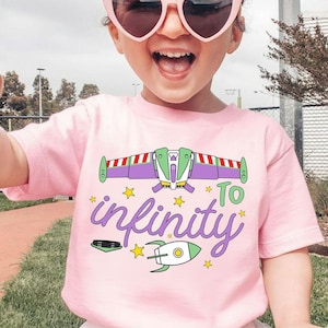 Puede incluir: Una camiseta rosa claro con un gr&aacute;fico colorido de una nave espacial y la frase "To infinity" en una fuente caprichosa. El dise&ntilde;o incluye estrellas y un cohete, creando un aspecto divertido. Esta camiseta infantil es perfecta para los fan&aacute;ticos del espacio y la aventura.