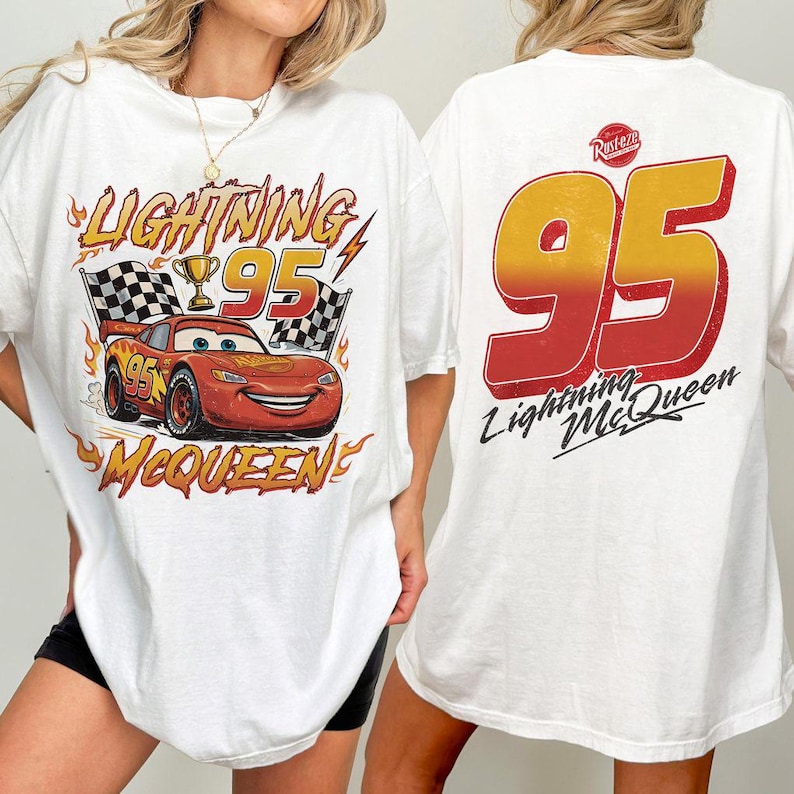 K&ouml;nnte beinhalten: Wei&szlig;es T-Shirt mit einer Grafik von Lightning McQueen aus dem Film Cars. Das Design auf der Vorderseite zeigt den Text "Lightning 95 McQueen" mit einem Cartoon-Auto, karierten Flaggen und einer Troph&auml;e. Auf der R&uuml;ckseite steht gro&szlig; "95" und "Lightning McQueen".