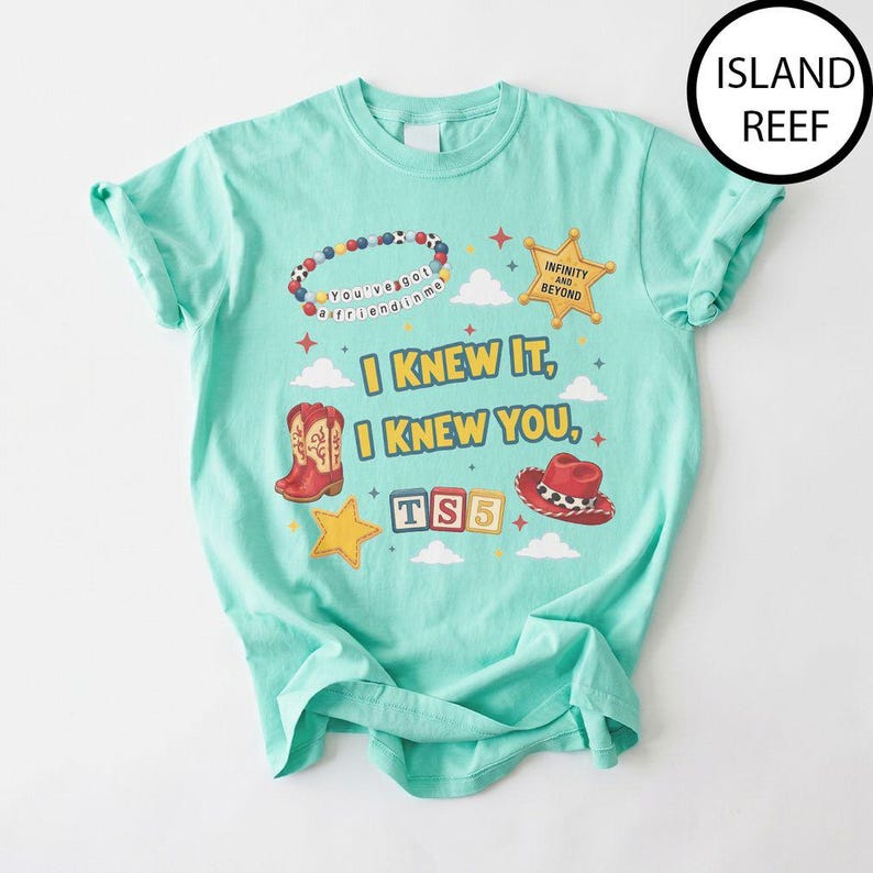 May include: A light mint green t-shirt featuring a graphic print with the text "I KNEW IT, I KNEW YOU," a beaded bracelet, a sheriff star badge with "INFINITY AND BEYOND," red cowboy boots, a red cowboy hat, and blocks labeled "TS5."