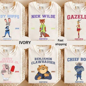 Könnte beinhalten: Elfenbeinfarbene T-Shirts mit Charakteren aus Zootopia. Jedes Shirt zeigt den Namen eines Charakters in einer College-Schriftart, zusammen mit dem Gründungsjahr und dem Zootopia-Logo. Zu den Charakteren gehören Judy Hopps, Nick Wilde, Gazelle, Jerry Jumbeaux Jr., Benjamin Clawhauser und Chief Bogo.