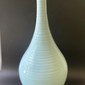 May include: A tall, slender ceramic vase with a pale, light blue glossy glaze. The vase features a bulbous base that tapers into a long, narrow neck, with a series of horizontal, raised ridges encircling the entire exterior surface from top to bottom.