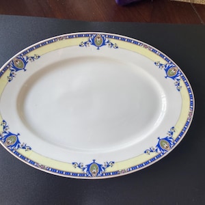 May include: Oval serving platter with a white center and a decorative border. The border features a yellow band with blue and green floral designs. The rim is trimmed with a thin blue and red line.