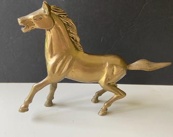 May include: A gold-colored brass horse figurine with a detailed mane and tail. The horse is in a running pose with its head turned to the side.