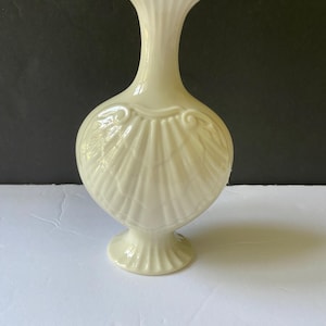 May include: A white porcelain vase with a gold rim and a shell design. The vase has a slender neck and a wide base.