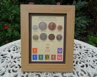 Puede incluir: Un marco de madera color roble claro que contiene una colección de monedas y sellos de 1956 del Banco de Inglaterra. La muestra presenta ocho monedas británicas antiguas etiquetadas y seis sellos coloridos con el monograma real ER y corona.