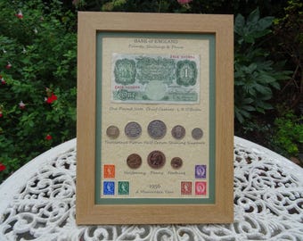 Puede incluir: Un marco que exhibe un billete de una libra del Banco de Inglaterra de 1956, varias monedas británicas incluyendo threepence, florin, half crown, shilling, sixpence, halfpenny, penny y farthing, además de seis sellos con la etiqueta 1956 A Memorable Year.