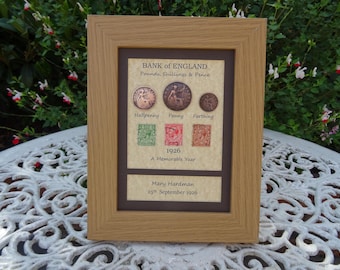 May include: A light wood-toned frame containing a display of 1926 British currency and stamps. The text reads Bank of England, Pounds, Shillings & Pence, Halfpenny, Penny, Farthing, 1926 A Memorable Year, Mary Hardman, and 25th September 1926.