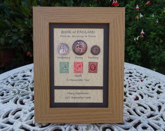 Puede incluir: Un marco de madera color roble claro que contiene tres monedas británicas antiguas etiquetadas como Halfpenny, Penny y Farthing, tres sellos postales, el texto Bank of England, 1926 A Memorable Year y Mary Hardman 25th September 1926.