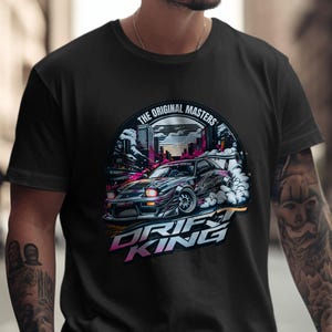 May include: Black t-shirt featuring a graphic of a drifting car with the text "DRIFT KING" in a stylized font. The design includes a cityscape and the words "THE ORIGINAL MASTERS".