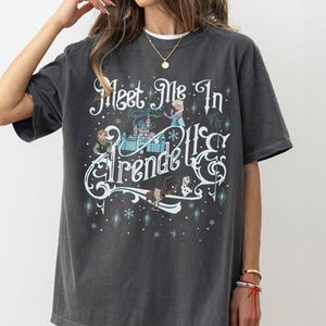 Könnte beinhalten: Dunkelgraues T-Shirt mit dem Text "Meet Me In Arendelle" in verspielter Schrift. Das Design zeigt ein Schloss, Figuren und Schneeflocken. Lässiger, übergroßer Schnitt.