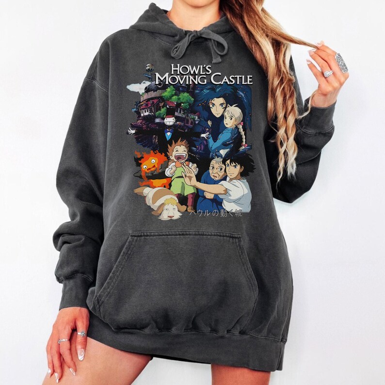 May include: Dark gray hoodie featuring a graphic from "Howl's Moving Castle." The design includes characters and the title in white. The hoodie has a drawstring hood and a front pocket.