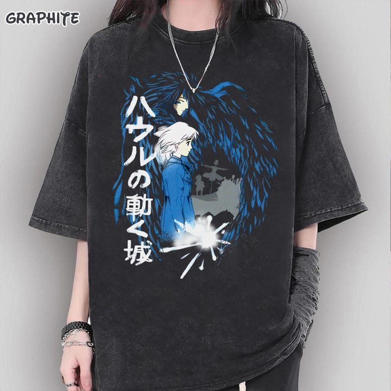 Puede incluir: Camiseta de color grafito con un dise&ntilde;o de "El castillo ambulante". El dise&ntilde;o incluye personajes en azul y blanco, con texto japon&eacute;s. La camiseta tiene mangas cortas y un corte holgado.