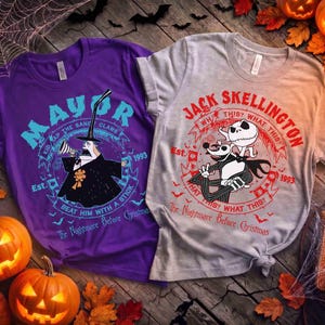 Op de afbeelding: Een paars t-shirt met de burgemeester uit The Nightmare Before Christmas met de tekst Mayor, Kidnap the Sandy Claws, Beat him with a stick, Est. 1993, en een grijs t-shirt met Jack Skellington en de tekst Jack Skellington, What this?