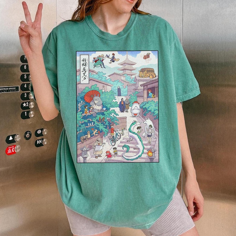 Puede incluir: Camiseta verde turquesa con una colorida ilustraci&oacute;n de estilo anime. El dise&ntilde;o muestra una escena callejera con varios personajes, edificios y un drag&oacute;n verde sinuoso. La camiseta es de estilo casual.