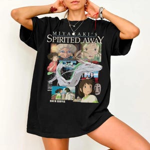 May include: Black t-shirt featuring a graphic design from the animated film "Spirited Away." The design includes the film's title, character illustrations, and Japanese text. The shirt is a crew neck style.