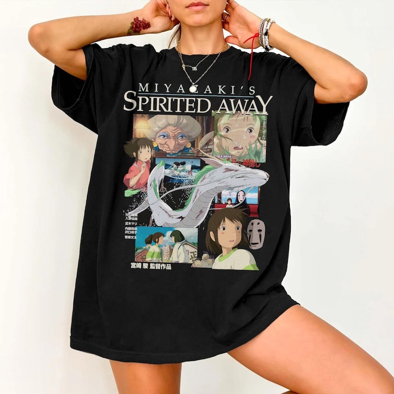 May include: Black t-shirt featuring a graphic design from the animated film "Spirited Away." The design includes the film's title, character illustrations, and Japanese text. The shirt is a crew neck style.